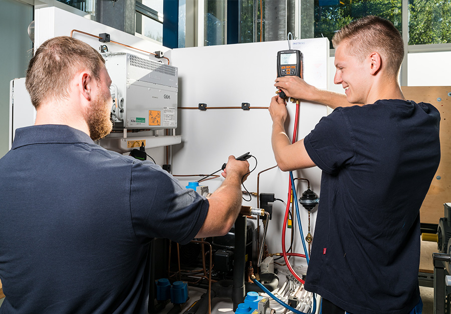 Das Foto zeigt einen Azubi der Instatec GmbH lächelnd bei der Arbeit und wird von seinem Vorgesetzten dabei betreut.