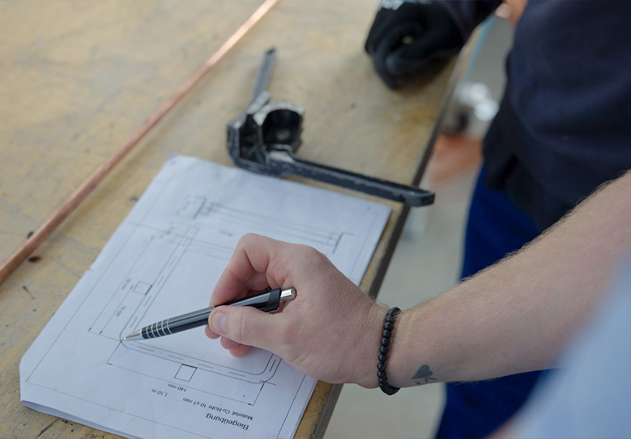 Das Foto zeigt die Besprechung für eine Biegeübung. Diese ist auf einem Blatt Papier als technische Zeichnung zu sehen.